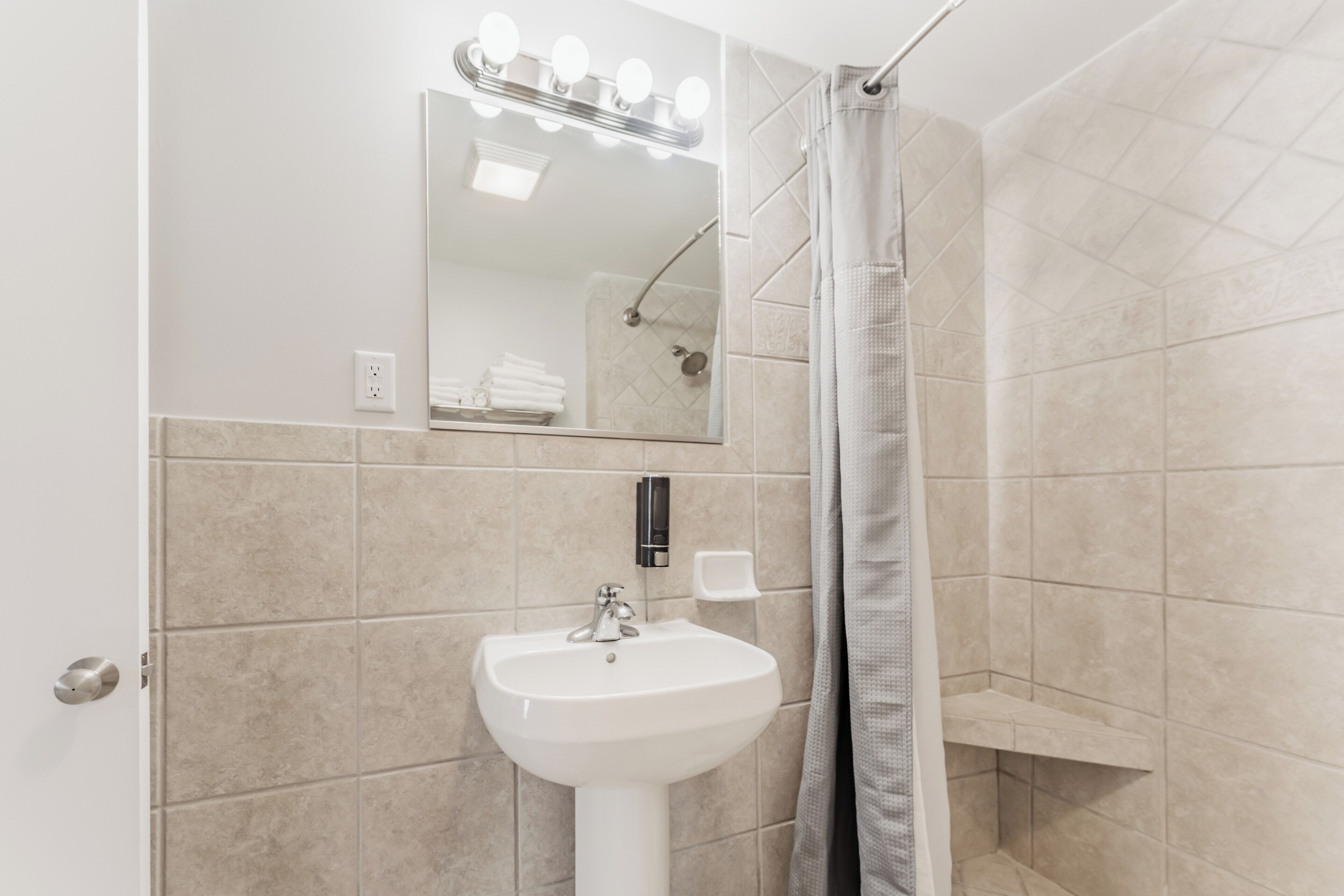 A bathroom with a sink, mirror, and shower.