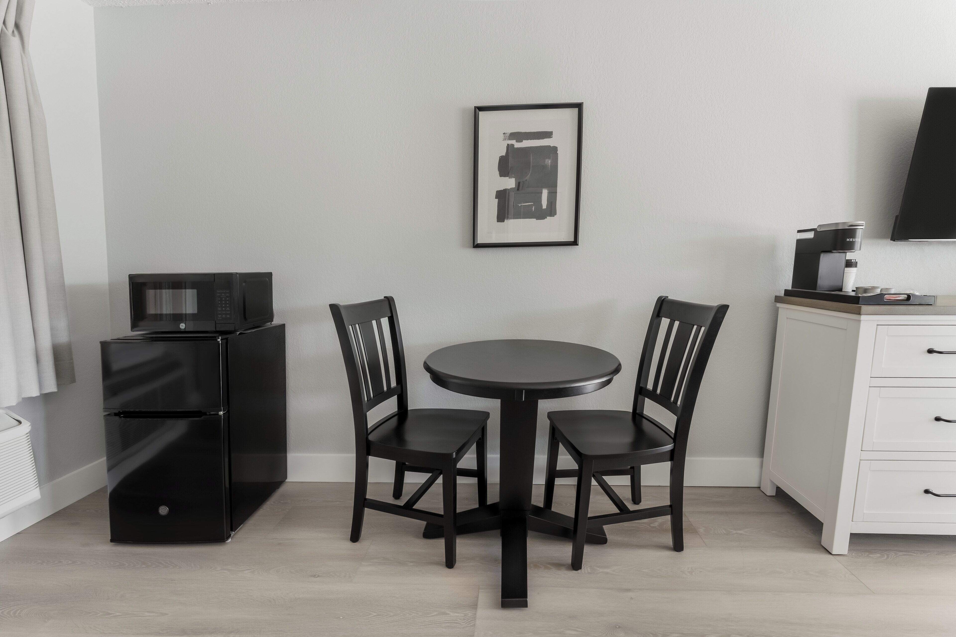 Une cuisine compacte avec un réfrigérateur noir, un four à micro-ondes, une machine à café et un meuble blanc.