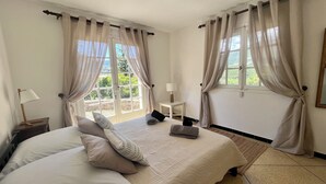 Camera da letto con un letto grande, due comodini, una finestra con tende e vista su del verde all'esterno.