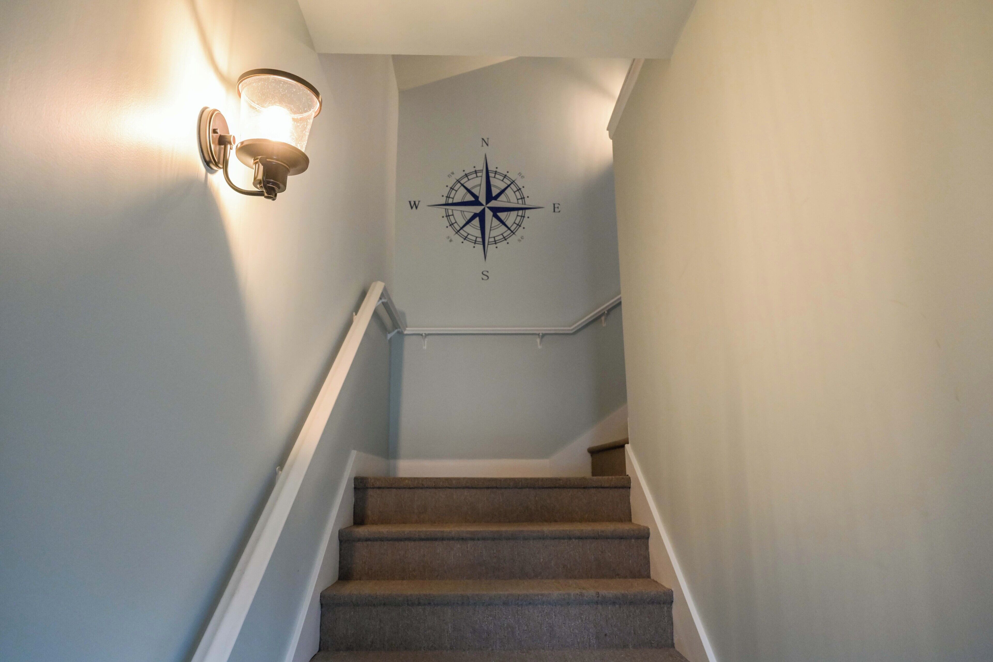 Un escalier orné d’un motif mural représentant une boussole, un luminaire sur le côté gauche et une main courante.