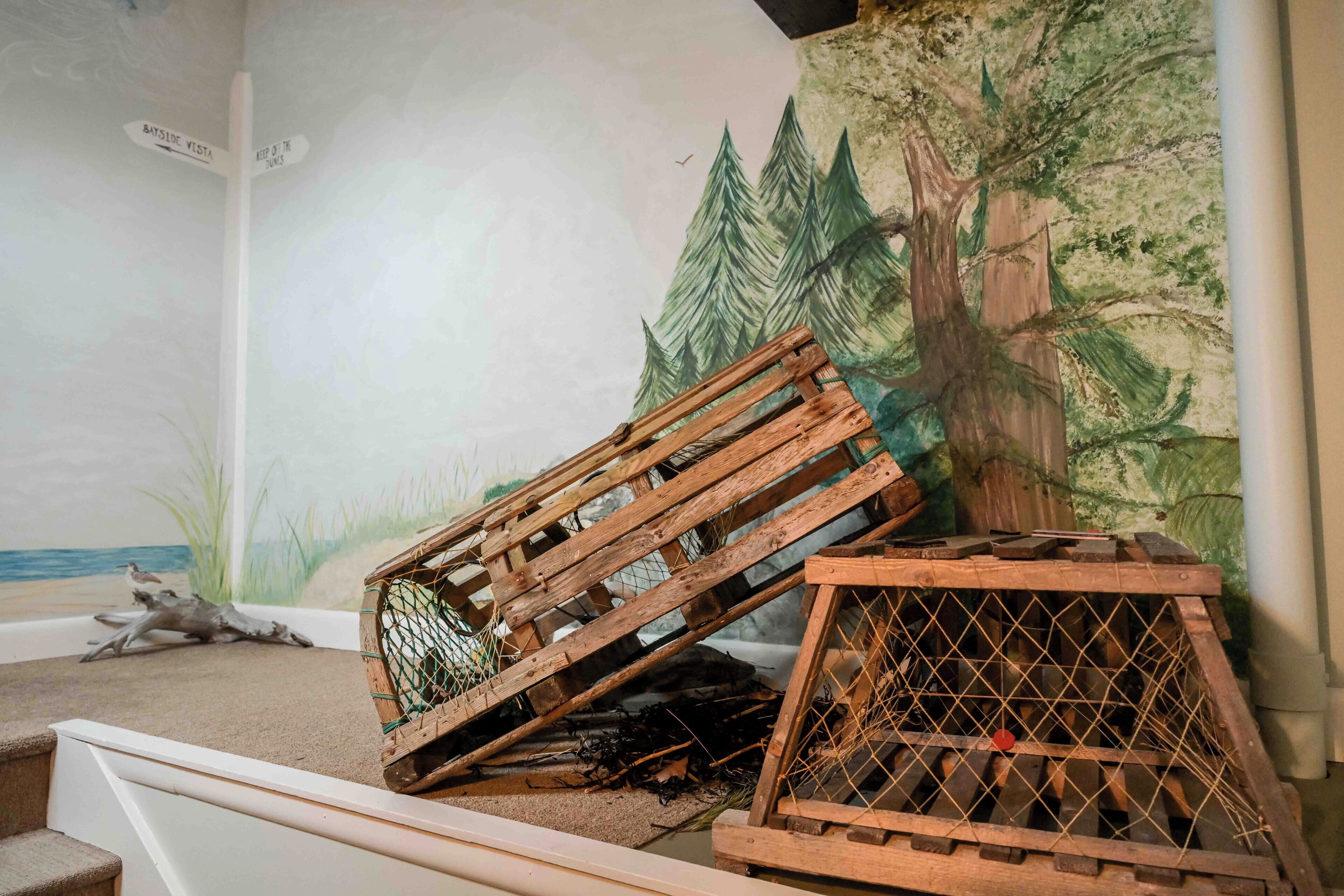 A room with a mural of a forest and a beach, a wooden crate, and a staircase.
