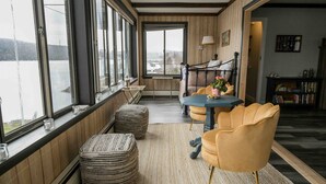 Una habitación acogedora con ventanas amplias, una cama, una mesa con sillas y una estantería.