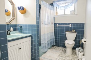 A bathroom with blue tiles, a white sink, a toilet, a shower curtain, and a window with a lace curtain.