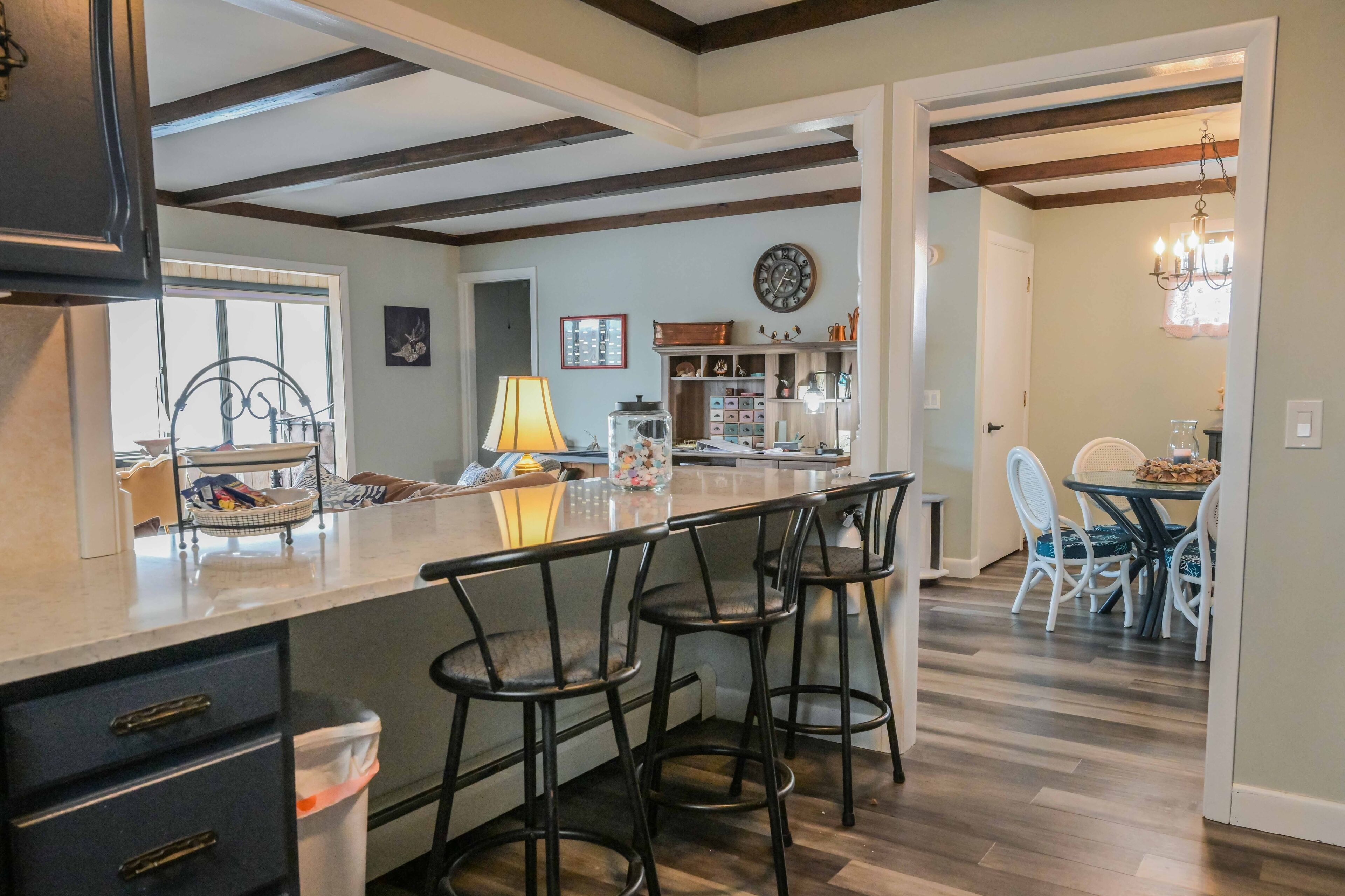 A kitchen with a central island, bar stools, and a dining area with chairs.
