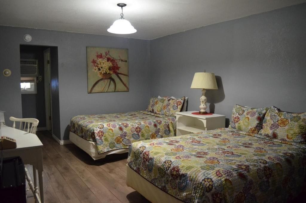 Una habitación con dos camas, un escritorio, una silla y una lámpara.