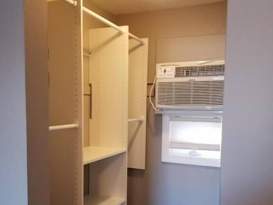 Um closet amplo com prateleiras abertas, uma luminária no teto e um aparelho de ar condicionado.