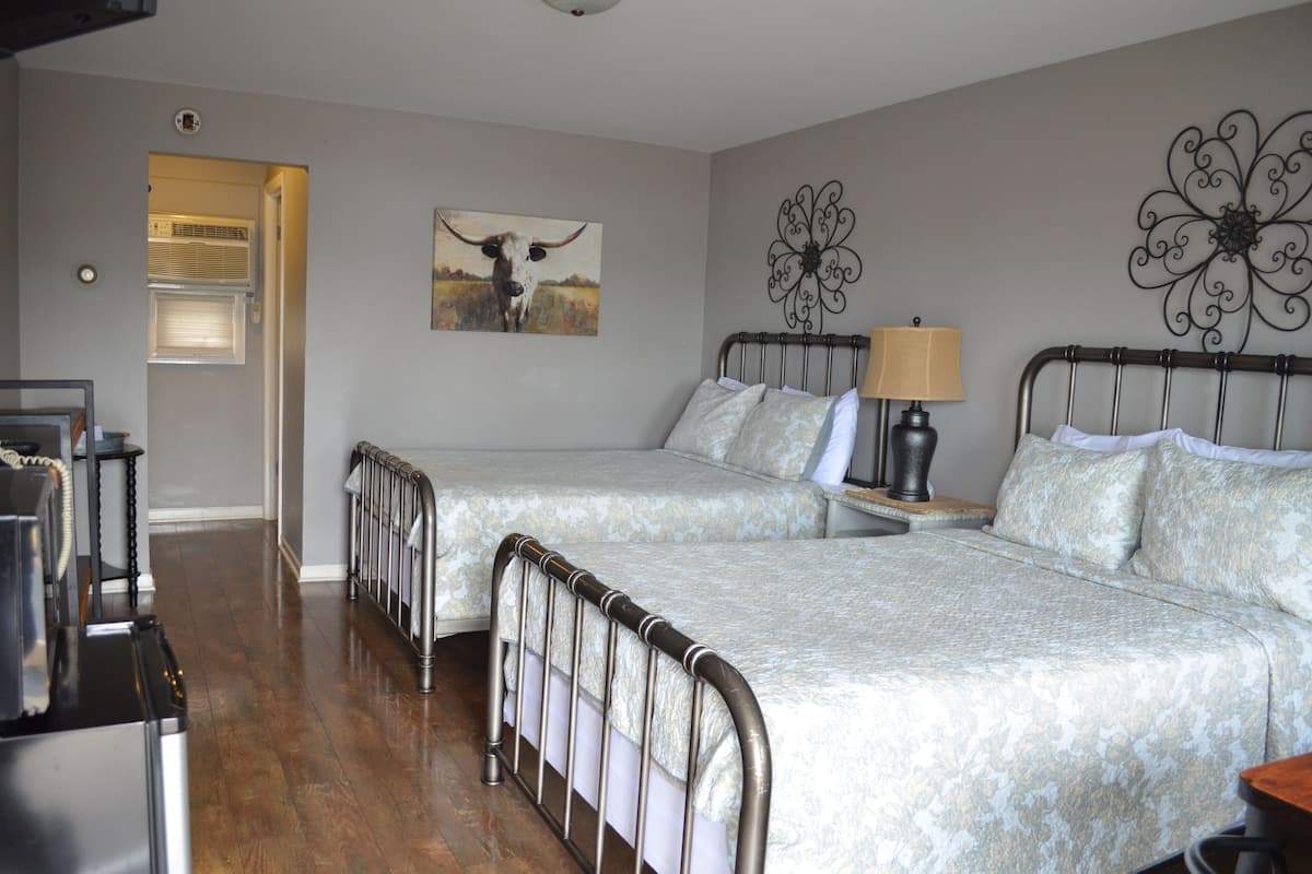 A bedroom with two beds, a bedside table with a lamp, a decorative wall piece, and a window with blinds.