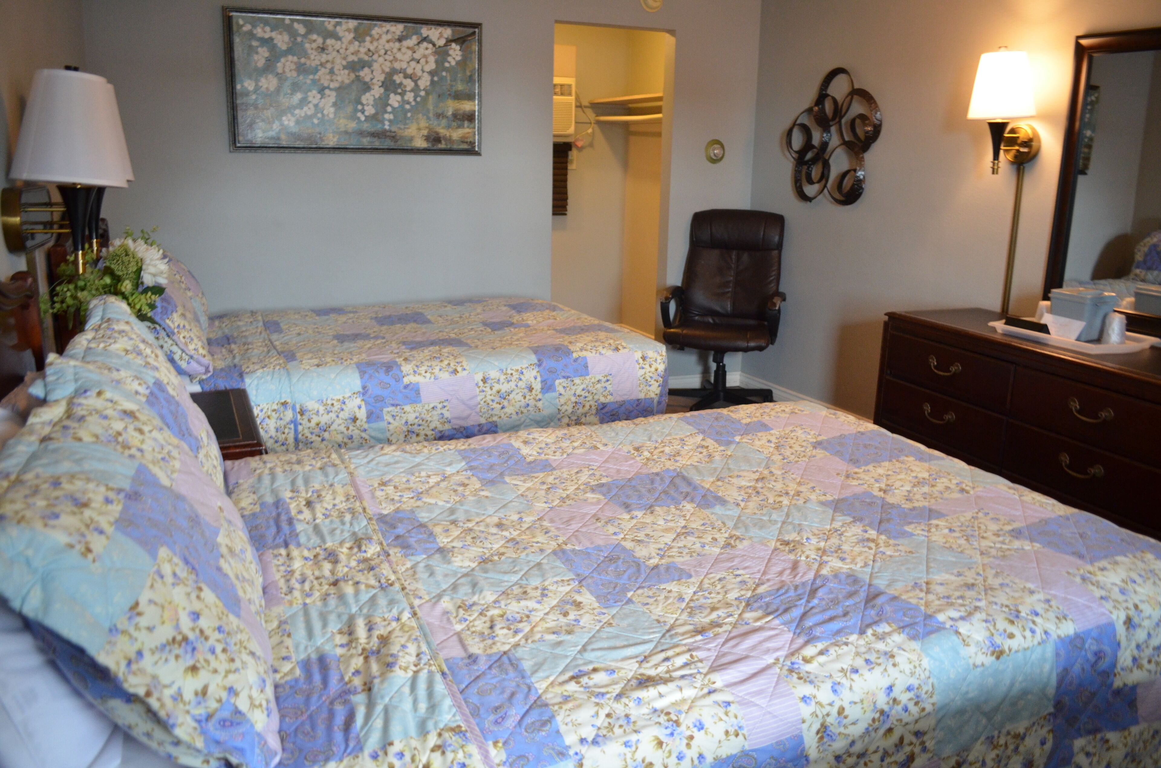 Habitación de hotel con dos camas, una silla, cómoda, lámpara, un cuadro y un espejo.