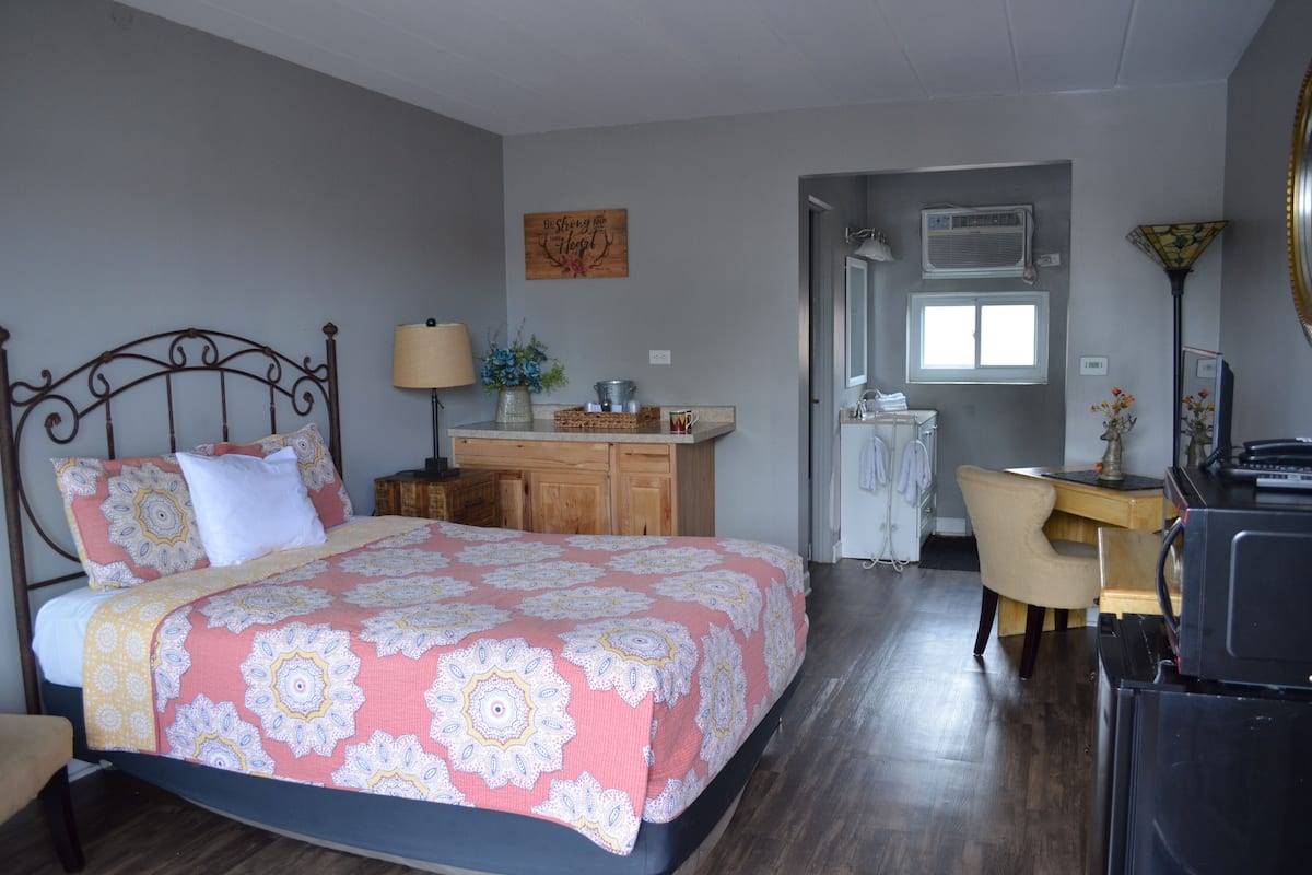 A bedroom with a bed, a desk, a chair, and a small kitchenette.
