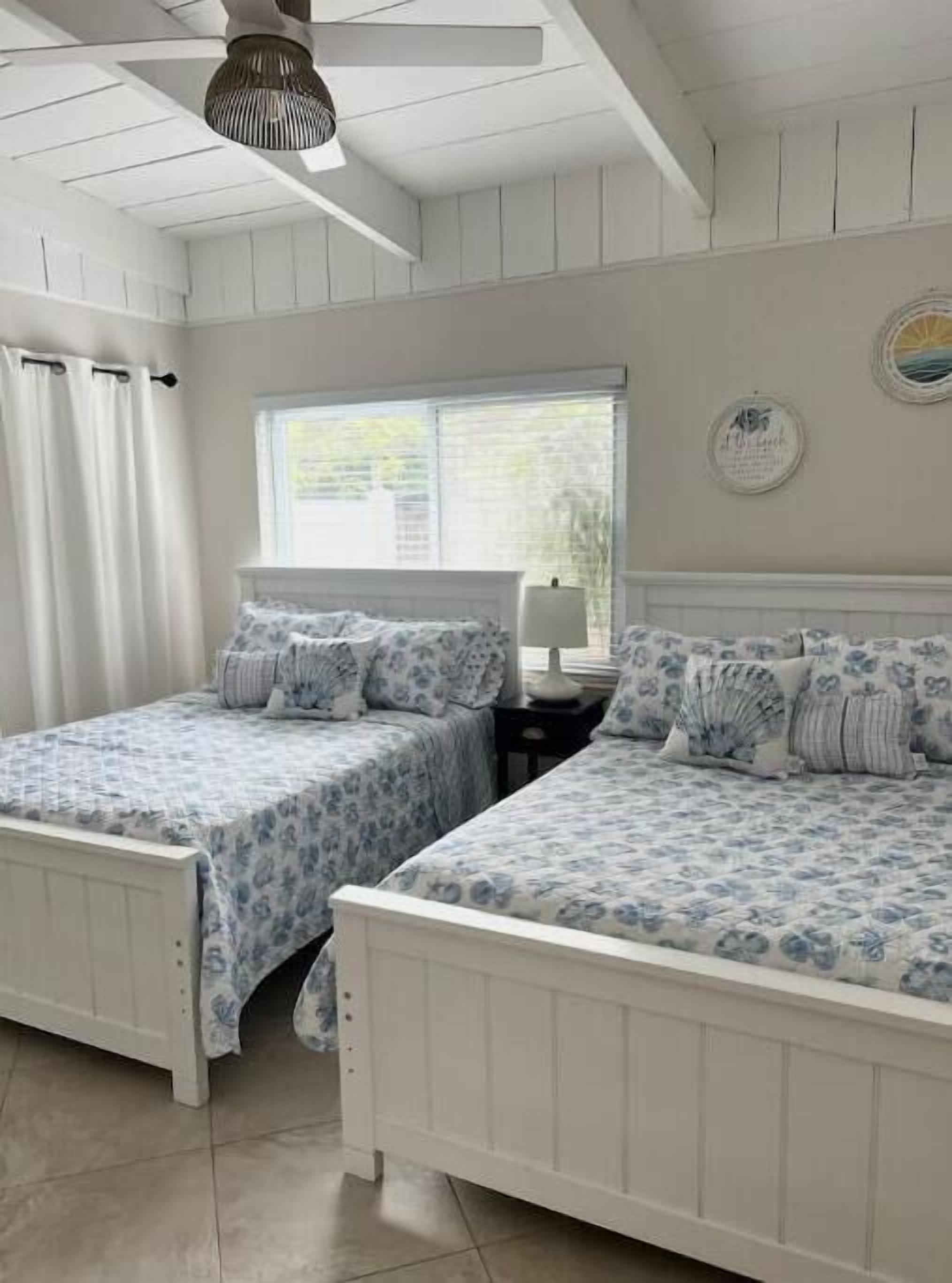 Une chambre avec deux lits, un ventilateur de plafond, une fenêtre avec des rideaux et une horloge murale.