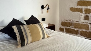 Een slaapkamer met een bed, kussens, een wandlamp en een bakstenen muur.