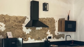 Een keuken met een modern design, voorzien van een zwarte afzuigkap, houten kastjes, een zwart aanrecht en een ingebouwde magnetron.