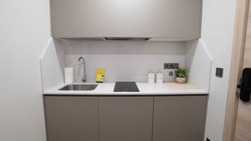A compact kitchen with a built-in sink, a faucet, a yellow bottle, and a small potted plant on the countertop.