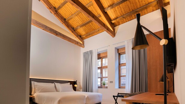 A bedroom with a bed, a desk, and a window with curtains. - Prisma Suites (Salamanca)