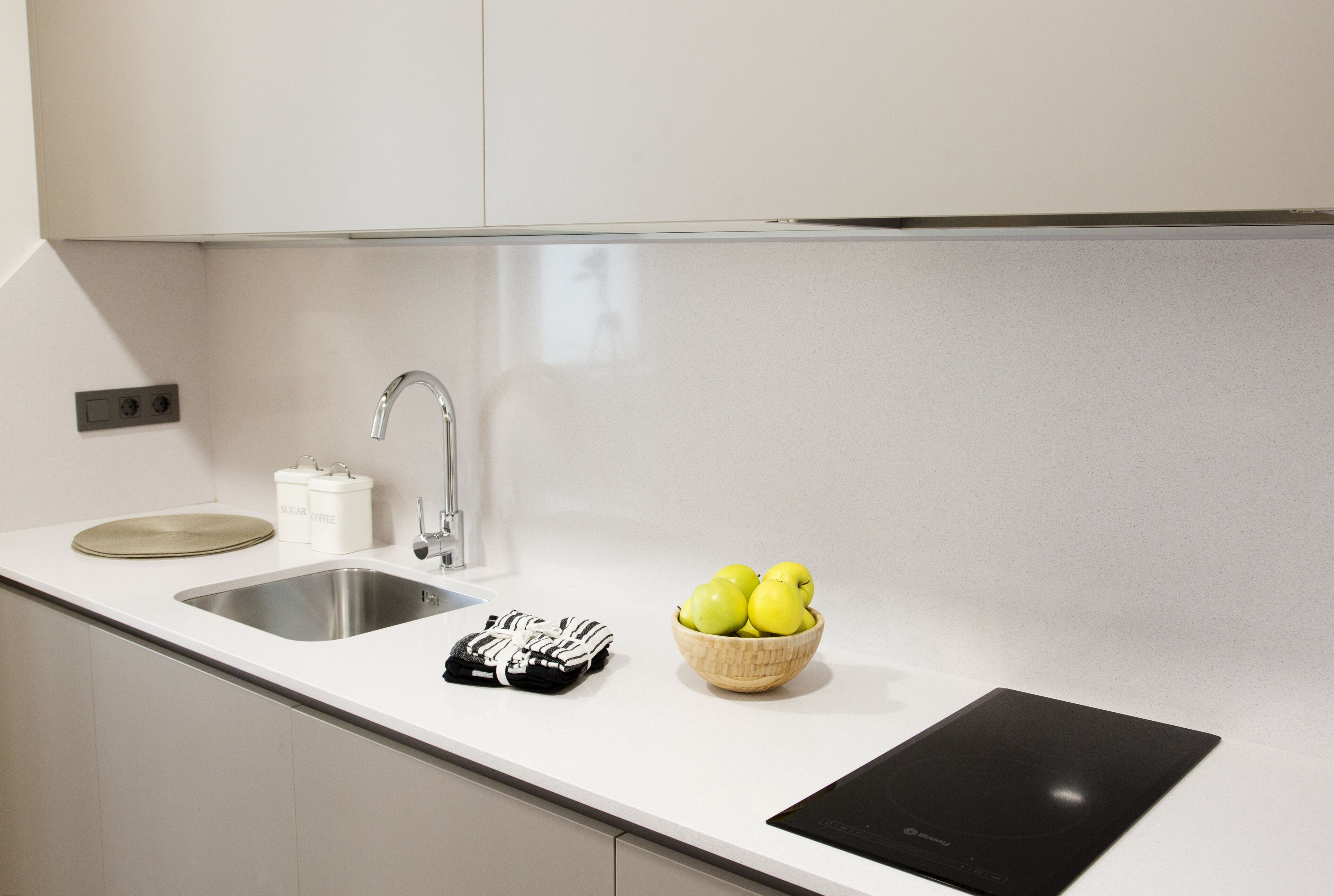 A modern kitchen with a stainless steel sink, a black induction cooktop, and a bowl of green apples on the counter.