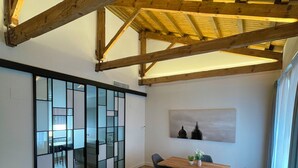 A spacious living area with a high ceiling and exposed wooden beams, a sliding glass door leading to a dining area, a dark blue sofa, and a wooden coffee table. - Prisma Suites (Salamanca)