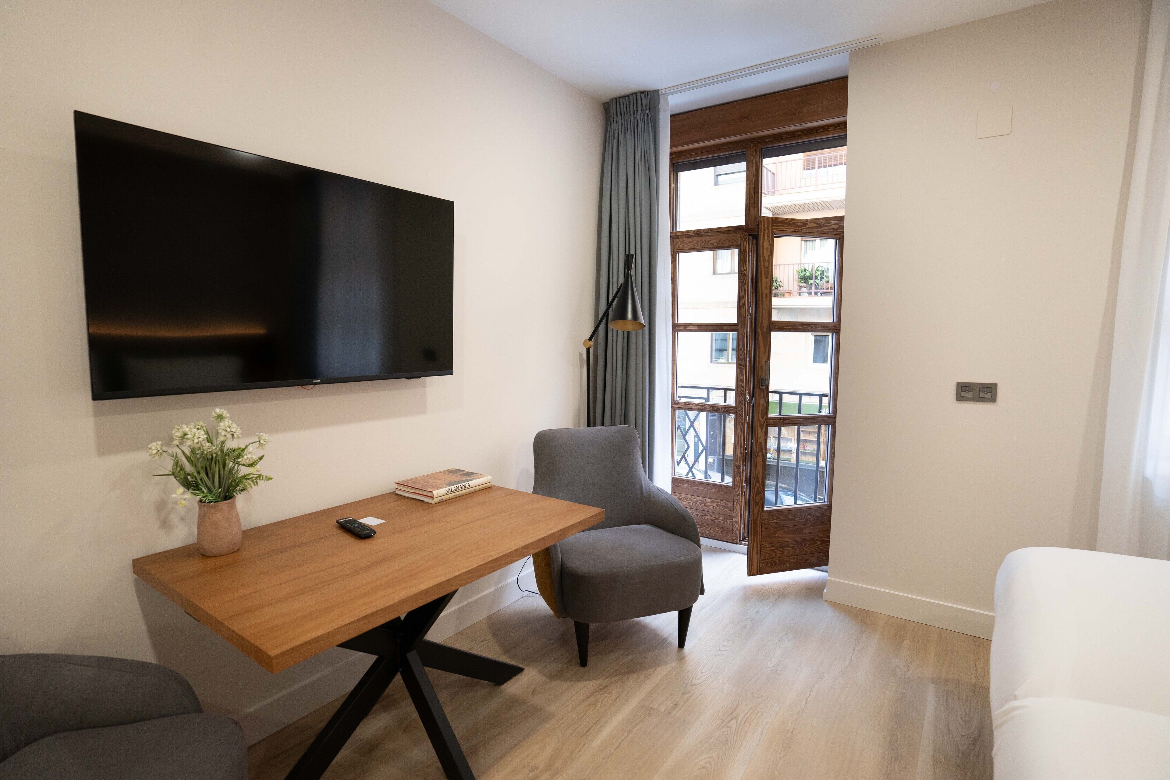 Un salon moderne avec un téléviseur à écran plat, une table en bois, un fauteuil gris et un canapé blanc.