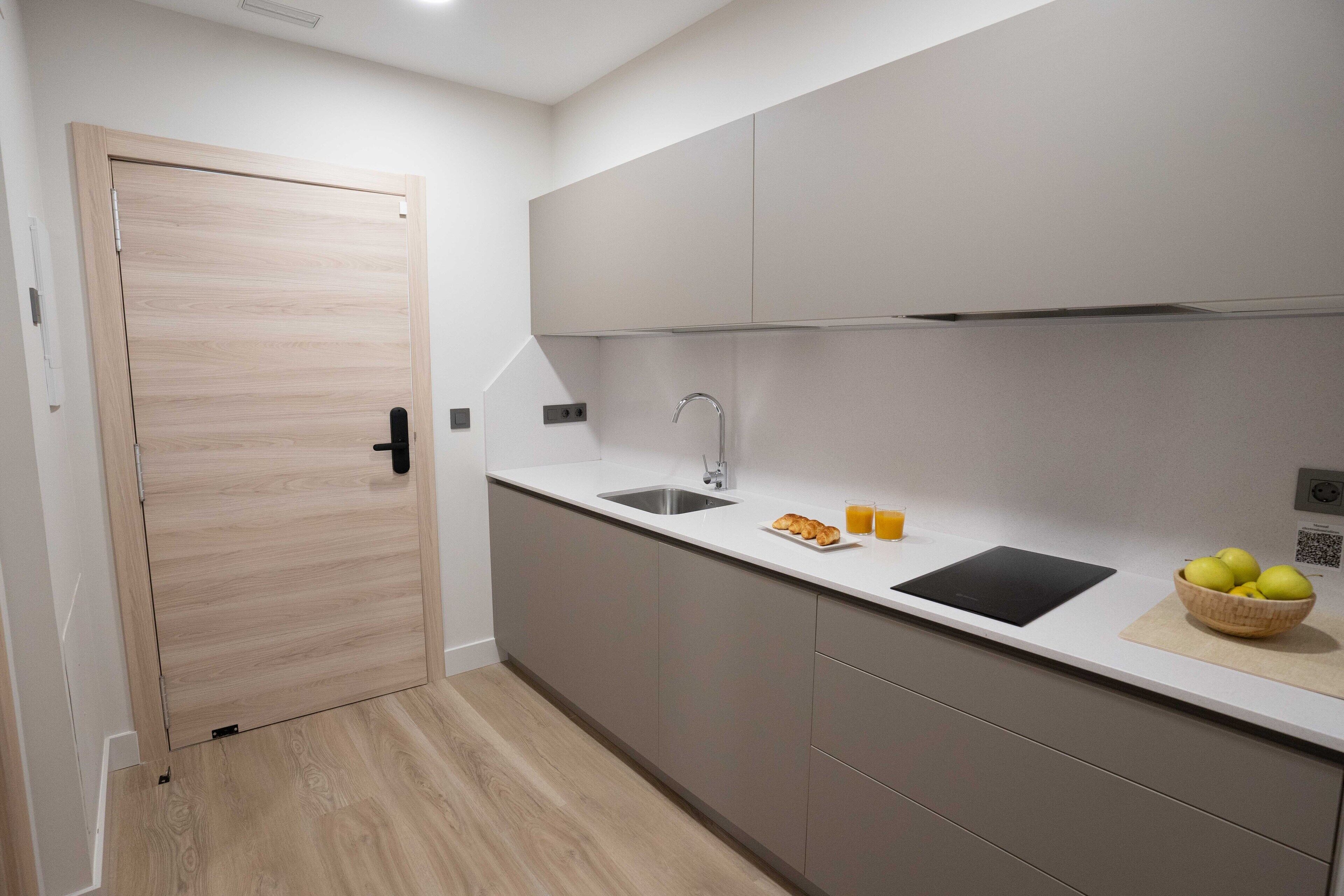 Una cocina moderna con puerta de madera, un lavabo, encimera negra y un bol de fruta.