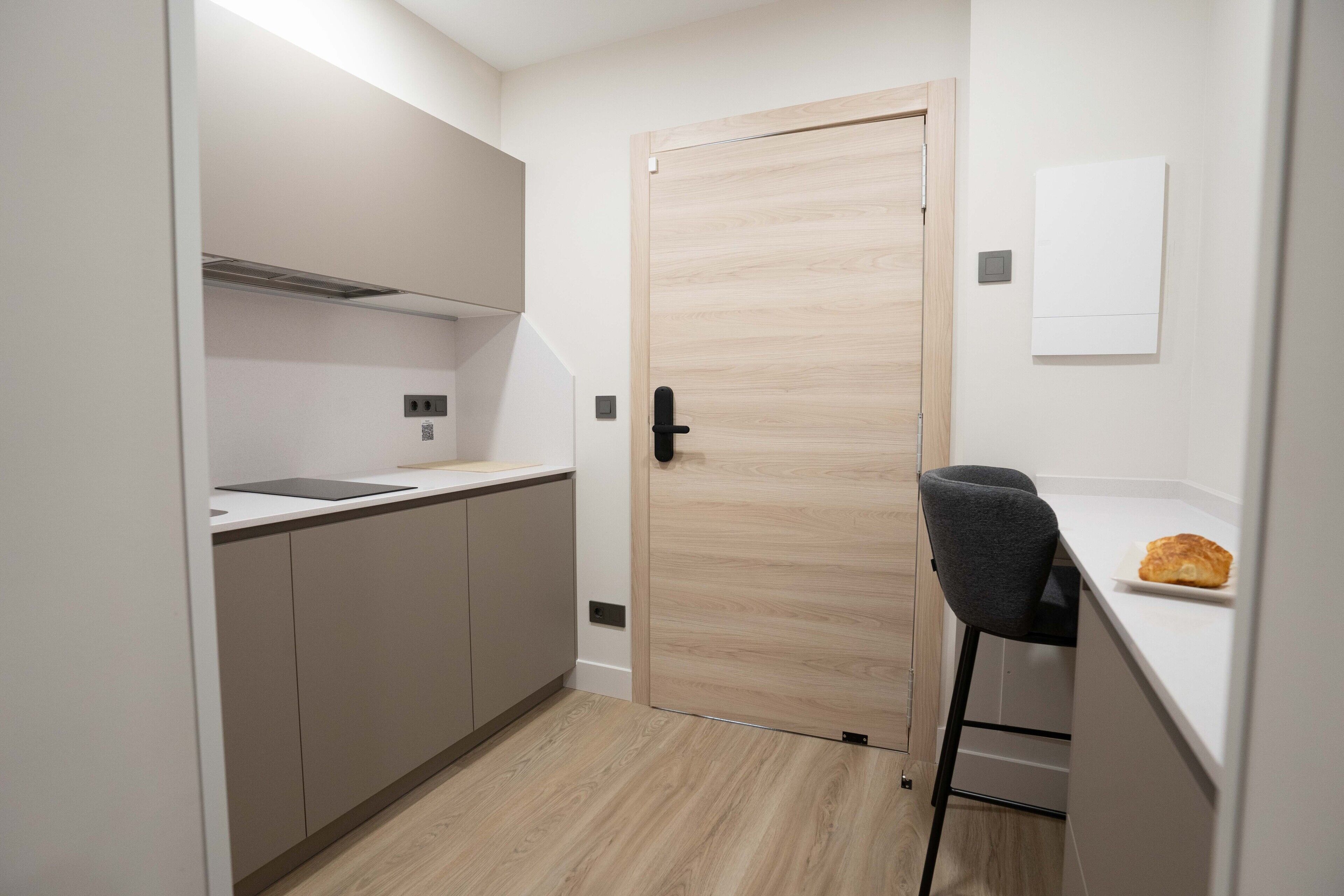 Cocina compacta con puerta de madera, un taburete y una pequeña barra.