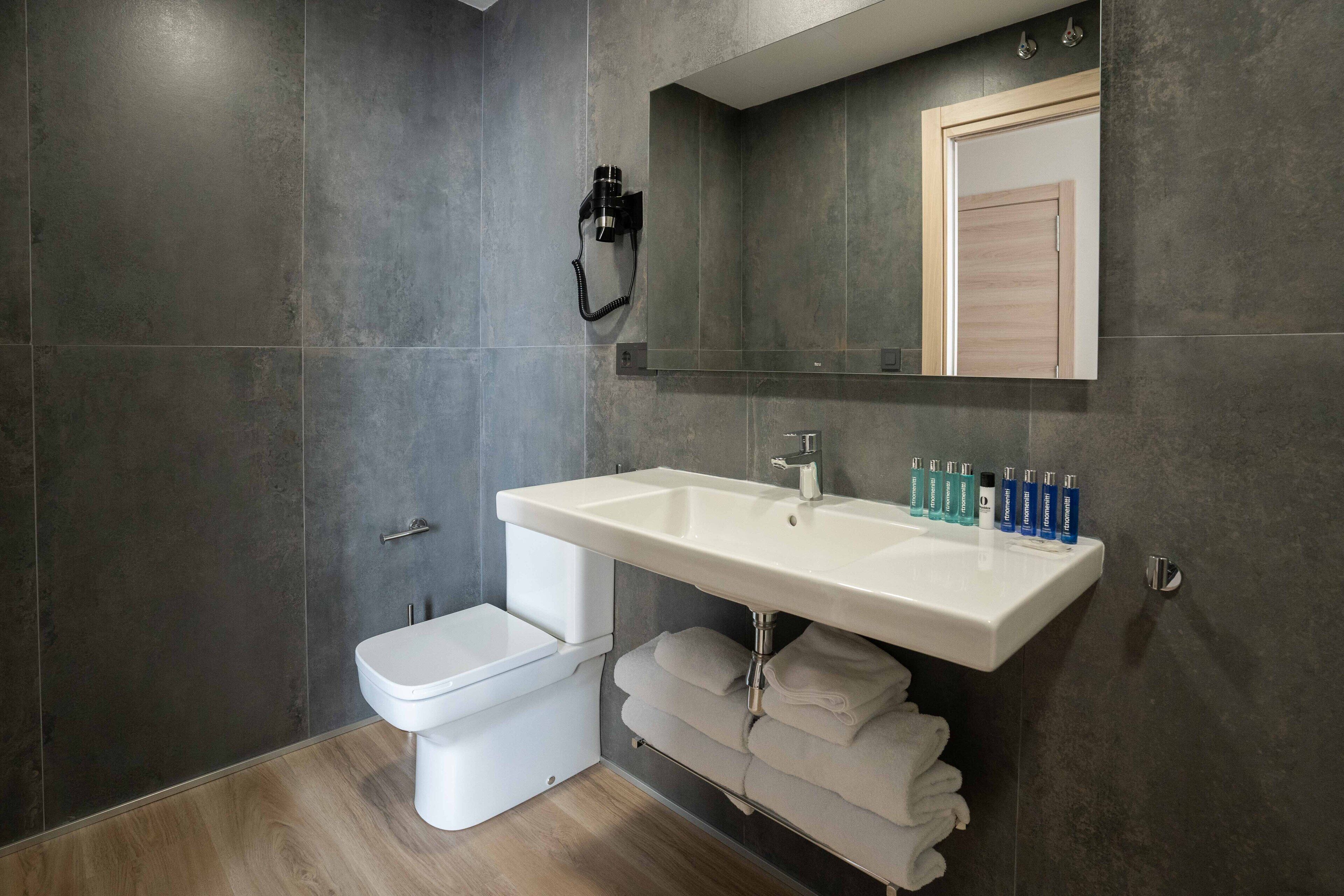 A modern bathroom with a white sink, a toilet, and a large mirror.