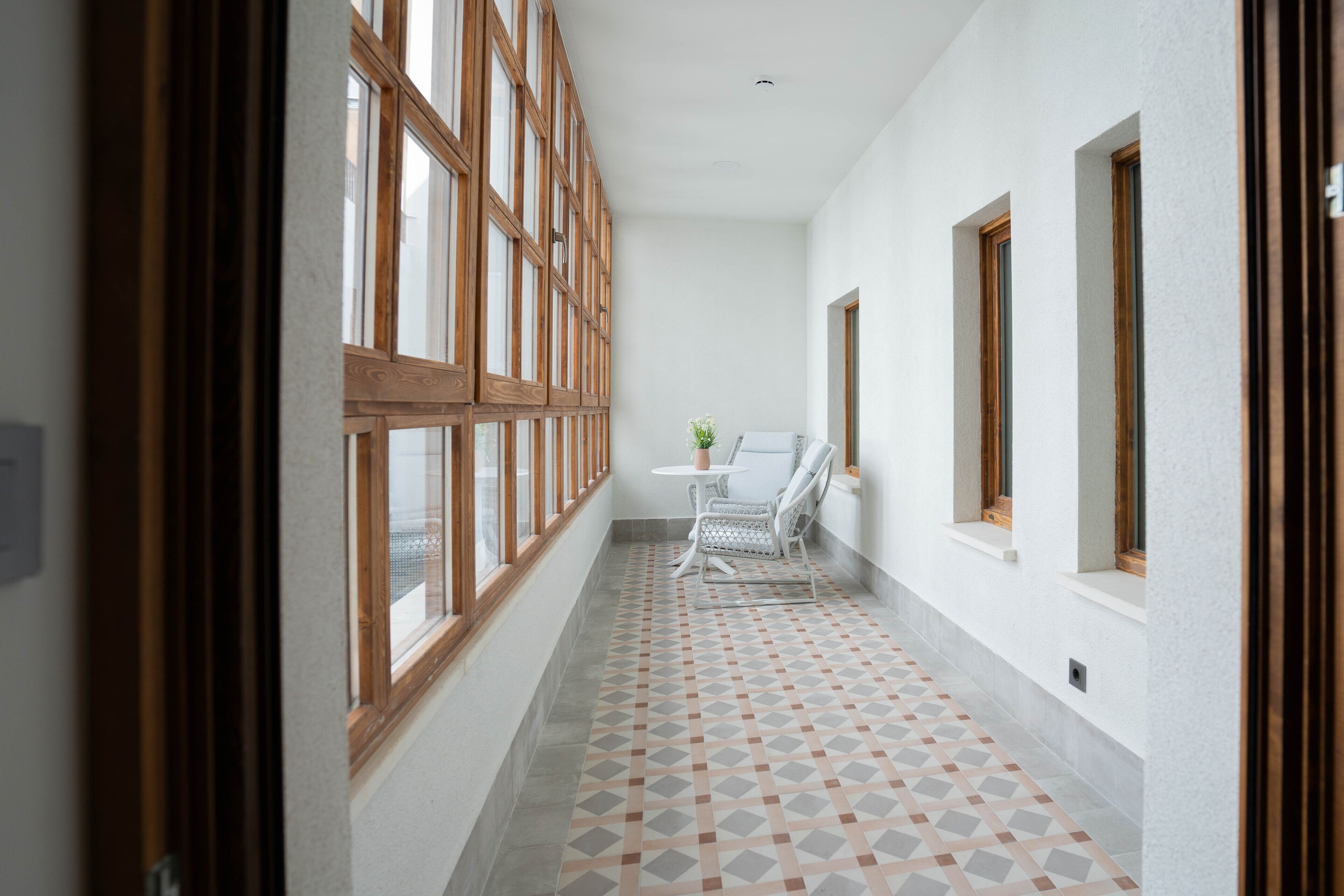 A corridor with patterned flooring, a white chair, and a table with a vase.