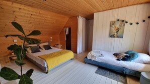 Ein gemütliches Schlafzimmer mit Holzboden, einem Bett mit gelber Decke, einem weiteren Bett mit blauen Kissen und einer großen Pflanze.