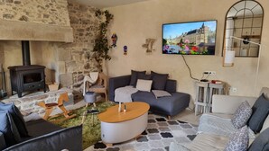 Ein gemütliches Wohnzimmer mit Steinwand, Kamin, großem Fernseher und bequemen Sitzmöglichkeiten.