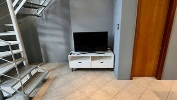 Un intérieur moderne avec un escalier, un téléviseur à écran plat posé sur un meuble blanc et un tapis à motifs géométriques.
