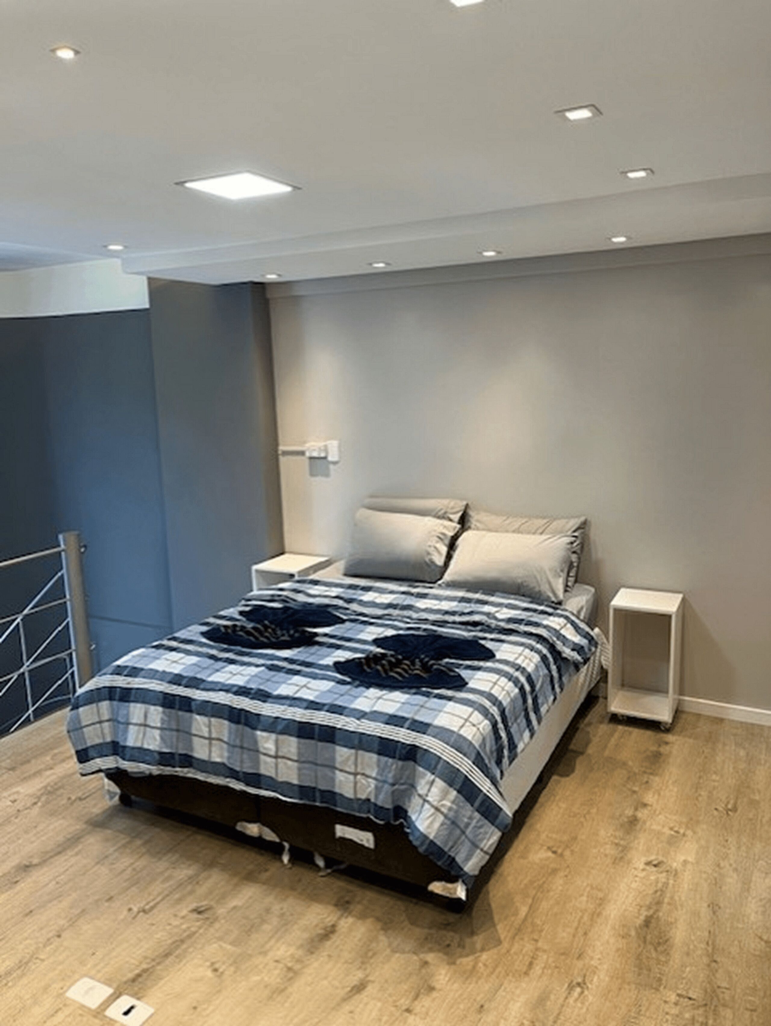 Quarto moderno com uma cama, mesas de cabeceira e uma pequena mesinha de apoio.