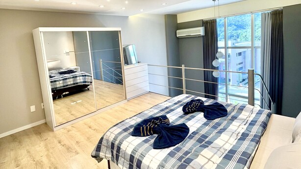 Un dormitorio moderno con una cama grande, un espejo y vistas de la ciudad a través de amplios ventanales.