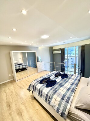 A modern bedroom with a large bed, a mirror, and a view of the city through large windows. - Saint Sebastian Flat 616Duplex no Centro (Jaragua do Sul)