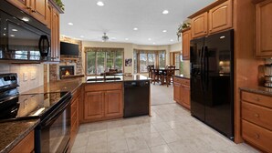 A spacious kitchen with wooden cabinets, a large island, a black refrigerator, and a stone fireplace. - Soft Landings at the Hangar House! Next to the Clubhouse and Airstrip (Danbury)