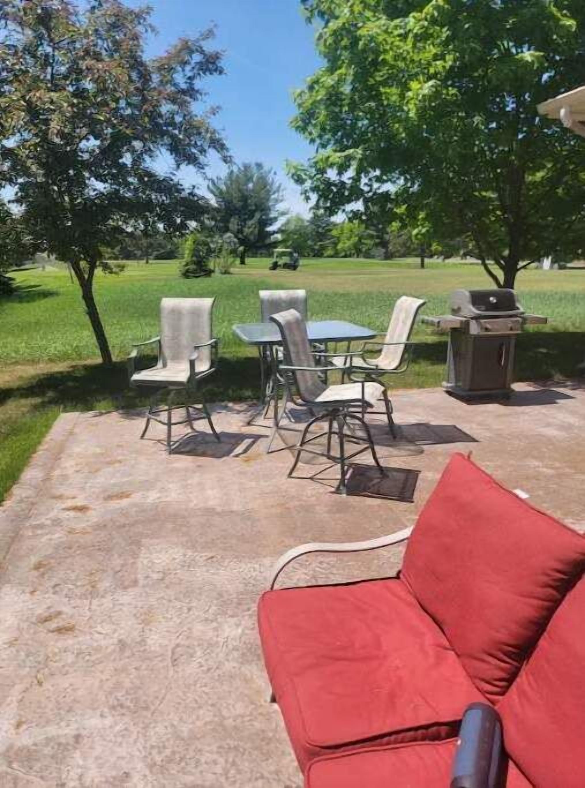 Un espacio al aire libre con un patio, un sofá rojo, sillas de metal y una mesa.