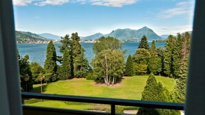 Une vue depuis une fenêtre donnant sur un lac, entouré d’arbres et de montagnes.