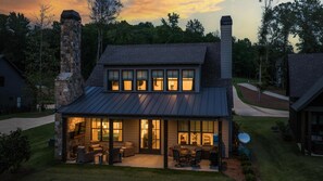 A two-story house with a stone chimney, a covered patio with outdoor furniture, and a well-maintained lawn.