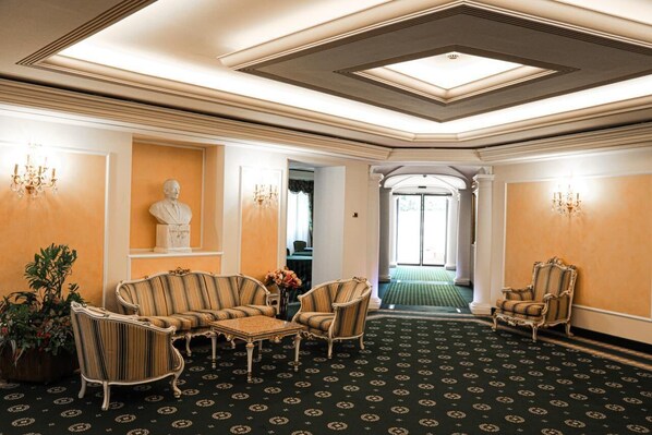 Un hall con alfombra estampada, sillones a rayas, una escultura de busto y un candelabro.