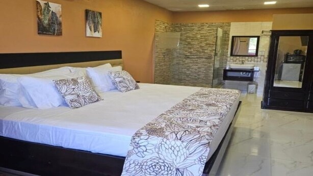 A hotel room with a large bed, a bathroom with a stone wall, and a mirror above the sink. - Beres Vale Apartments - King Room
 (Castara)