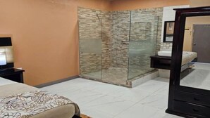 A hotel room with a bed, a bedside table, a mirror, a glass-enclosed shower, and a vanity with a sink. - Beres Vale Apartments - King Room
 (Castara)