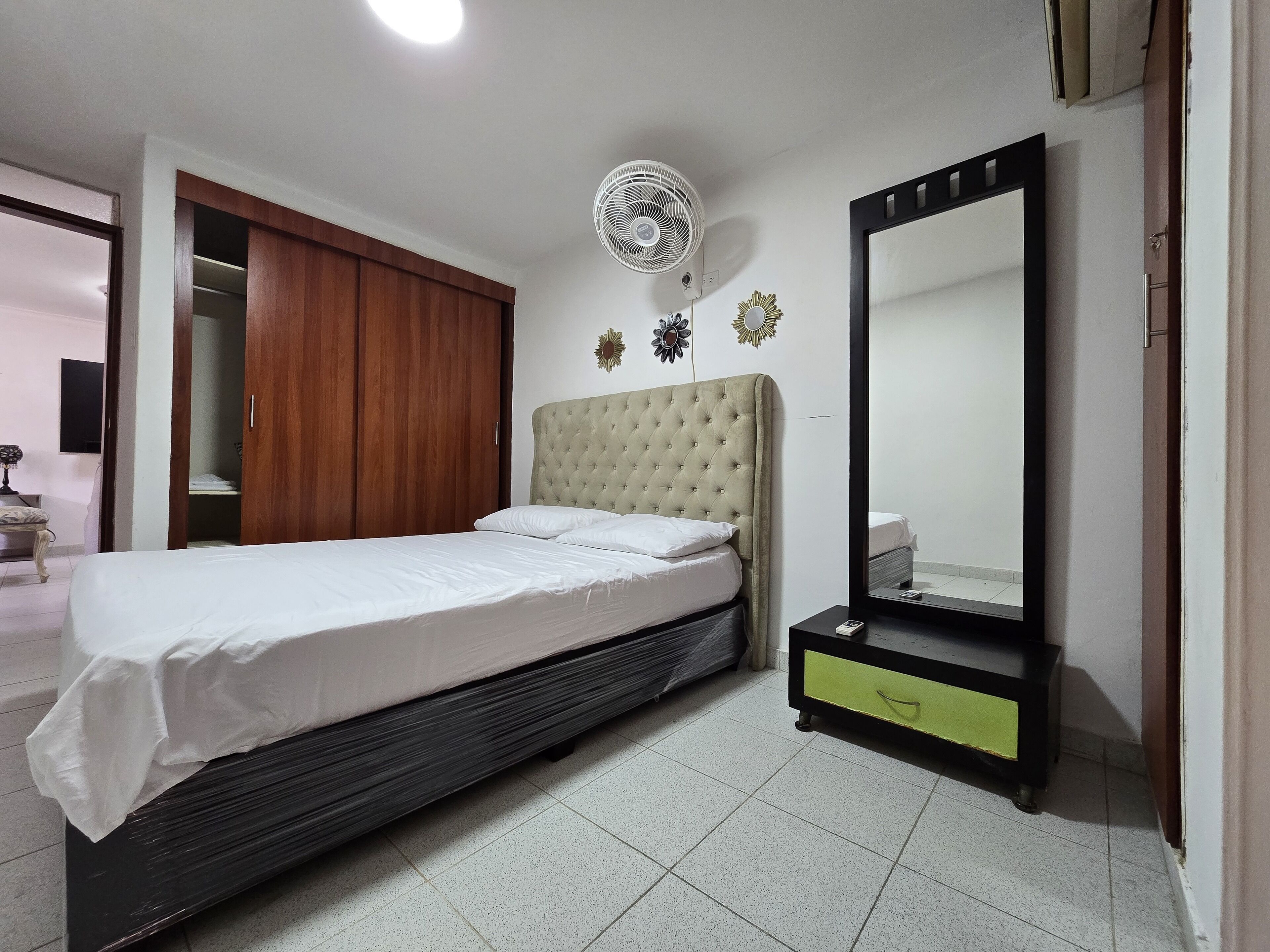 A bedroom with a bed, a bedside table, a mirror, and a wardrobe.