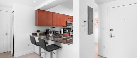 A modern kitchen with a bar area, featuring stainless steel appliances, wooden cabinets, and a white interior.