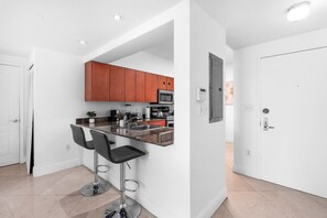 A modern kitchen with a bar area, featuring stainless steel appliances, wooden cabinets, and a white interior. - Spacious 2 Bed Unit in Brickell with Free Parking (Miami)