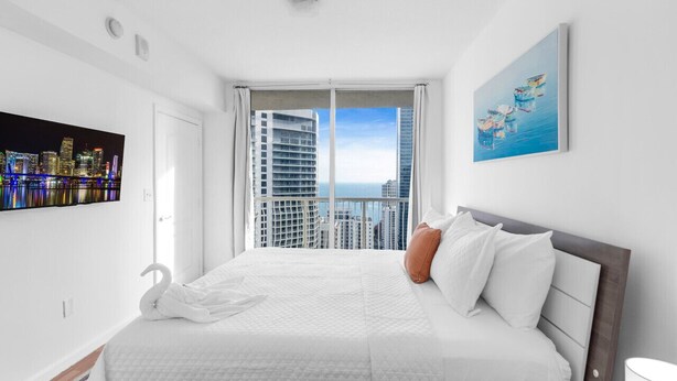 Habitación de hotel moderna con una cama grande, vistas de la ciudad desde un balcón y un cuadro en la pared.
