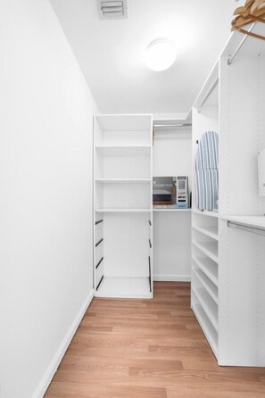 Un vestidor estrecho con estanterías blancas y suelo de madera.