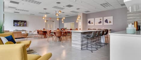 Un lobby moderno de hotel con un área central para comer, un bar y diferentes disposiciones de asientos.