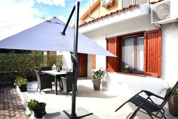An outdoor patio with a table and chairs, a large umbrella, and potted plants.