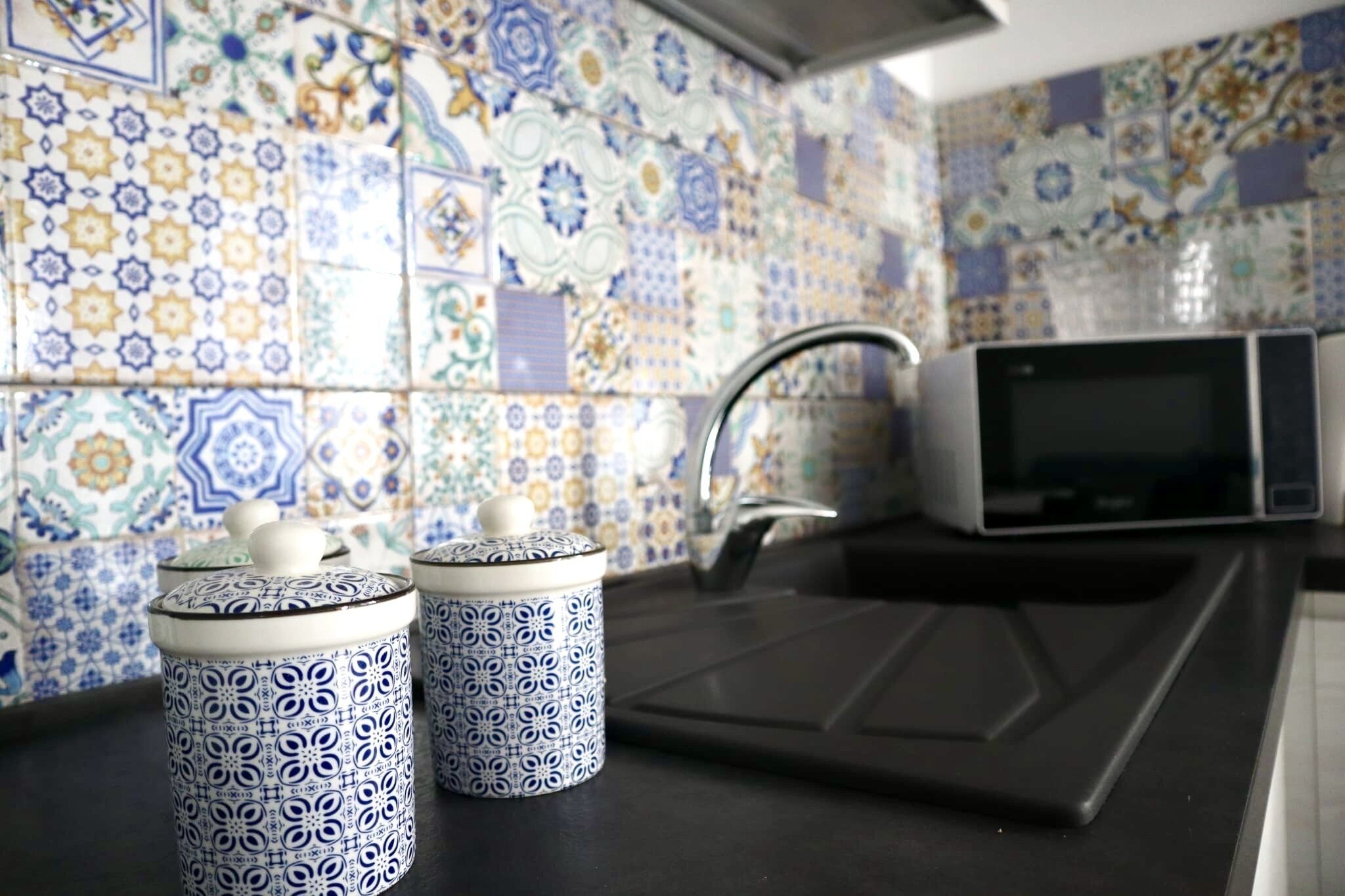 Une cuisine avec des carreaux décoratifs, un four à micro-ondes et deux récipients décoratifs.