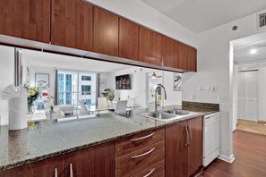 A modern kitchen with wooden cabinets, a granite countertop, a stainless steel sink, and a dishwasher. - Amazing 1 Bed in Brickell key W/ FREE PKG (Miami)