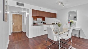 A modern kitchen with wooden cabinets, a microwave, and a coffee maker. There is a glass dining table with white chairs and a vase of flowers. - Amazing 1 Bed in Brickell key W/ FREE PKG (Miami)