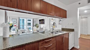 A modern kitchen with wooden cabinets, a granite countertop, and a dishwasher. - Amazing 1 Bed in Brickell key W/ FREE PKG (Miami)