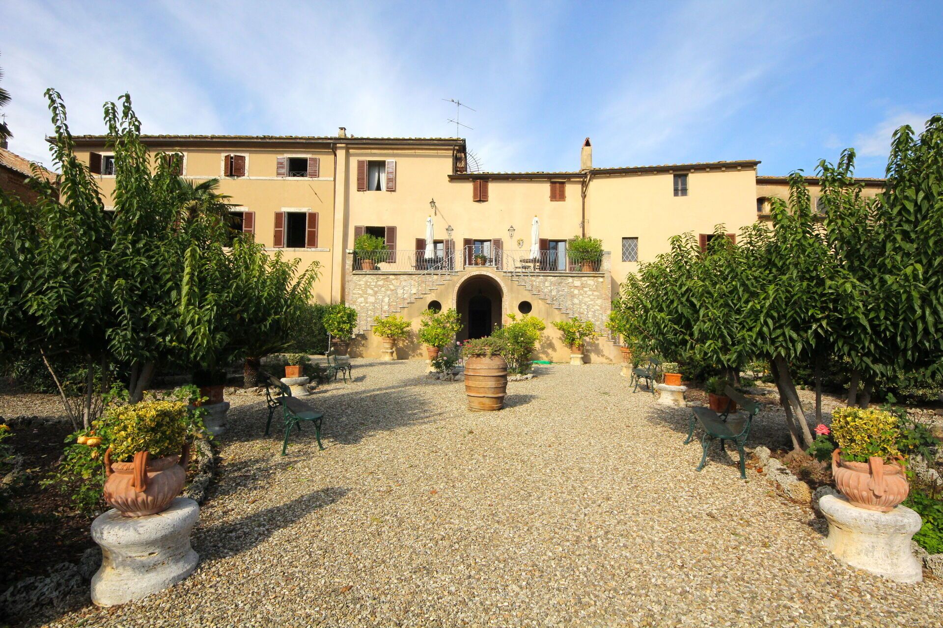 A courtyard with a building featuring a stone archway, potted plants, and outdoor seating.